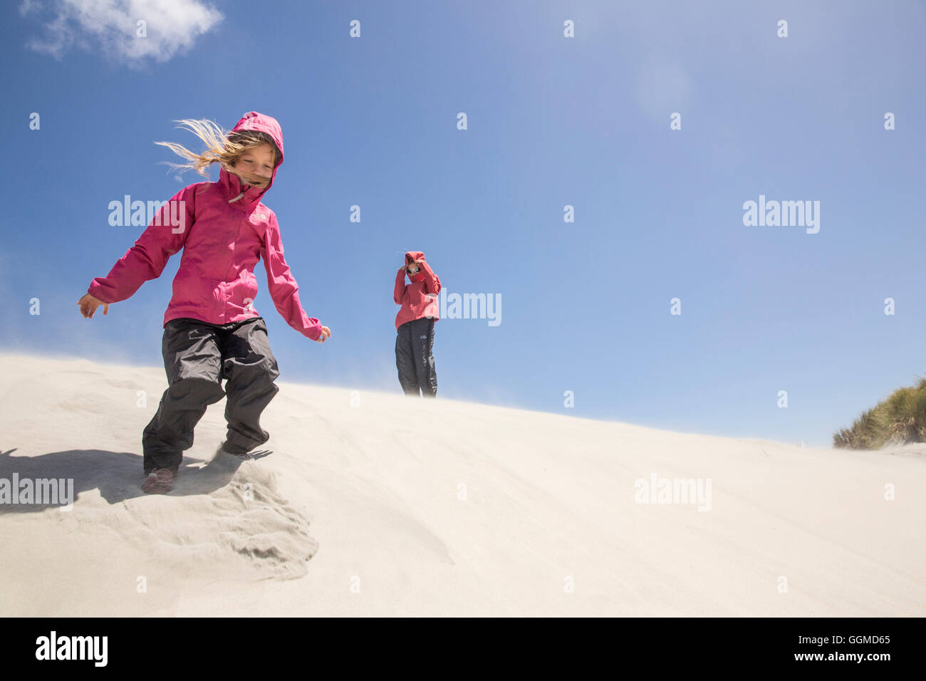 A girl in a sandstorm on the dunes of Wharariki Beach, Farewell Spit, South Island, New Zealand Stock Photo
