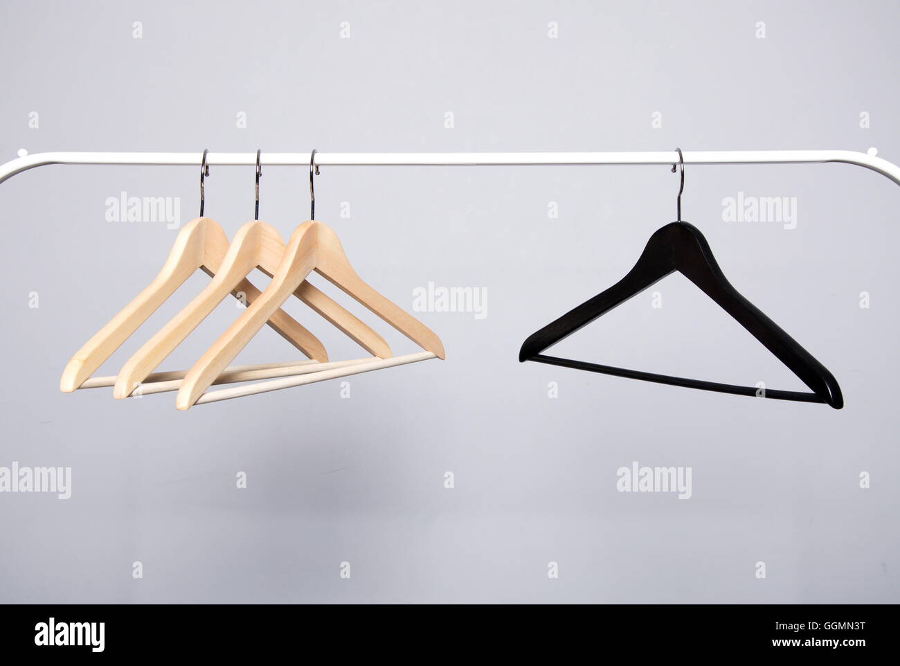 Three beige and one black clothes hangers hanging opposite each other on a white crossbar Stock Photo