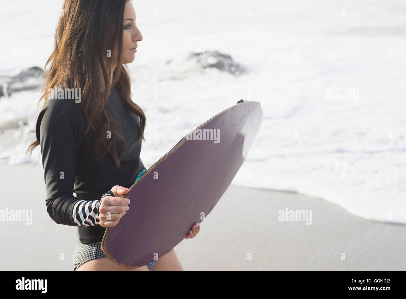 Caucasian woman holding skimboard at beach Stock Photo