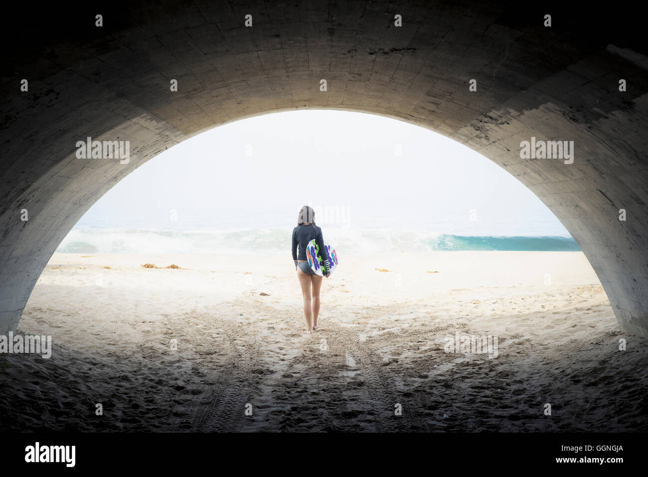 Caucasian woman carrying skimboard under arch Stock Photo
