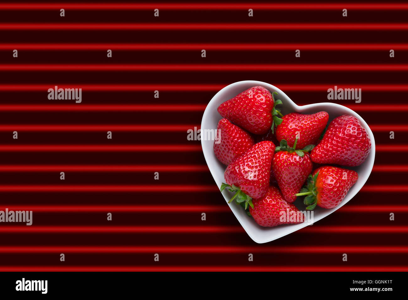 Strawberries in heart-shape bowl on red striped background Stock Photo