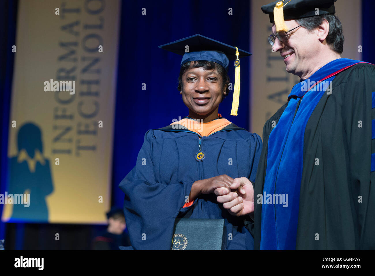 Graduation candidate in cap and gown receives diploma at Western Governors University commencement ceremony in Orlando, FL Stock Photo
