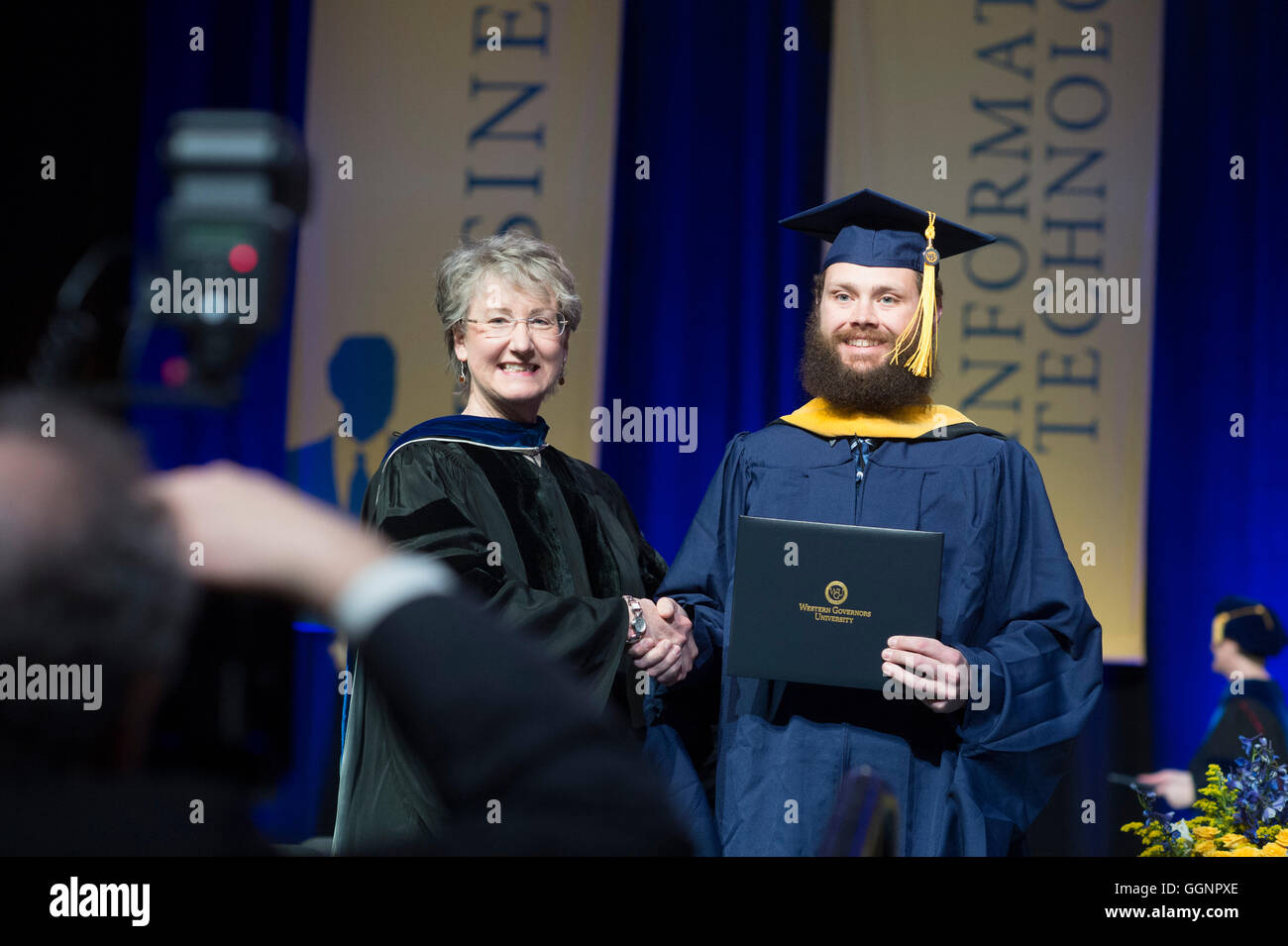 Graduation candidate in cap and gown receives diploma at Western Governors University commencement ceremony in Orlando, FL Stock Photo