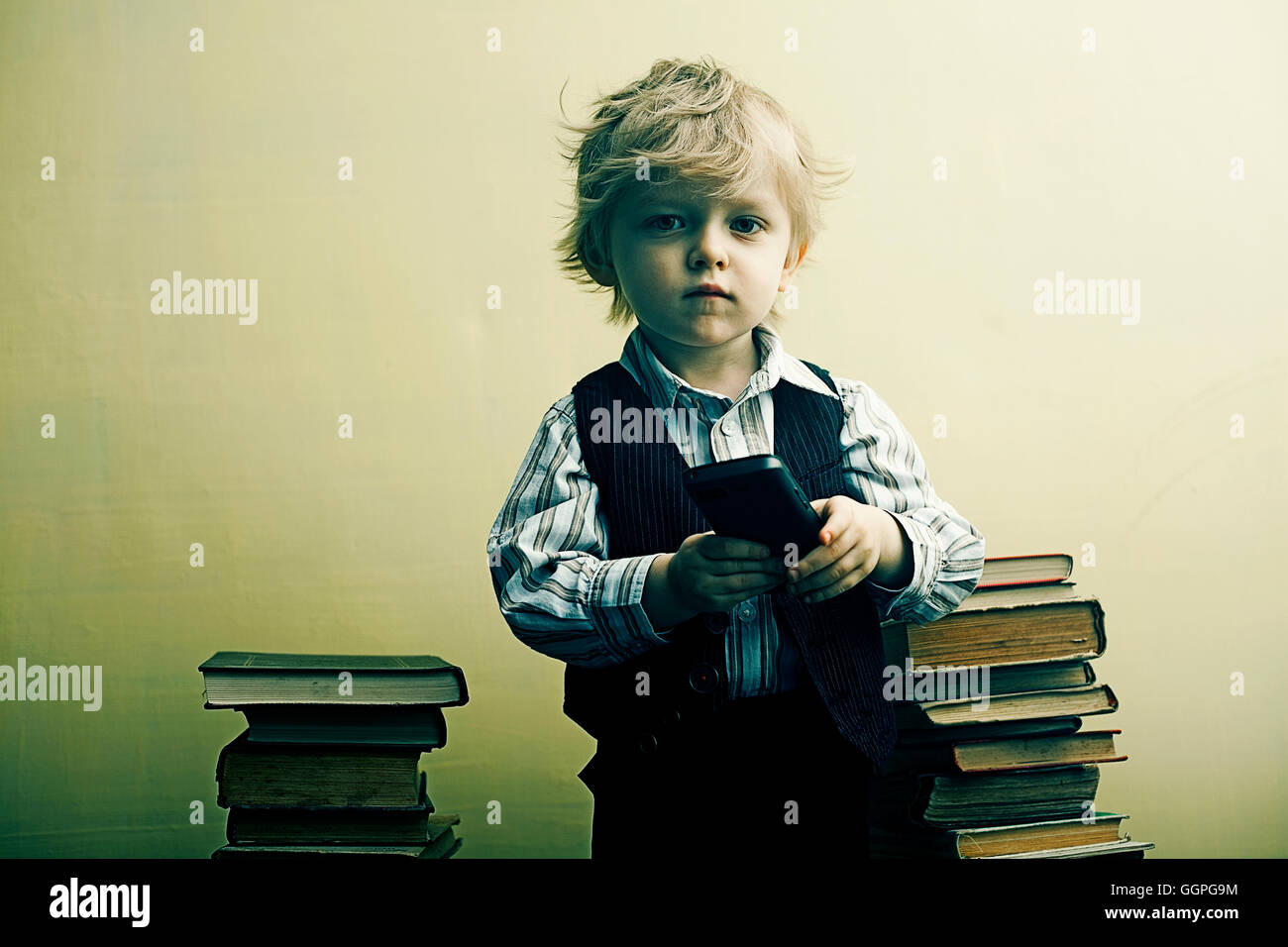 Boy holding cell phone near stacks of books Stock Photo