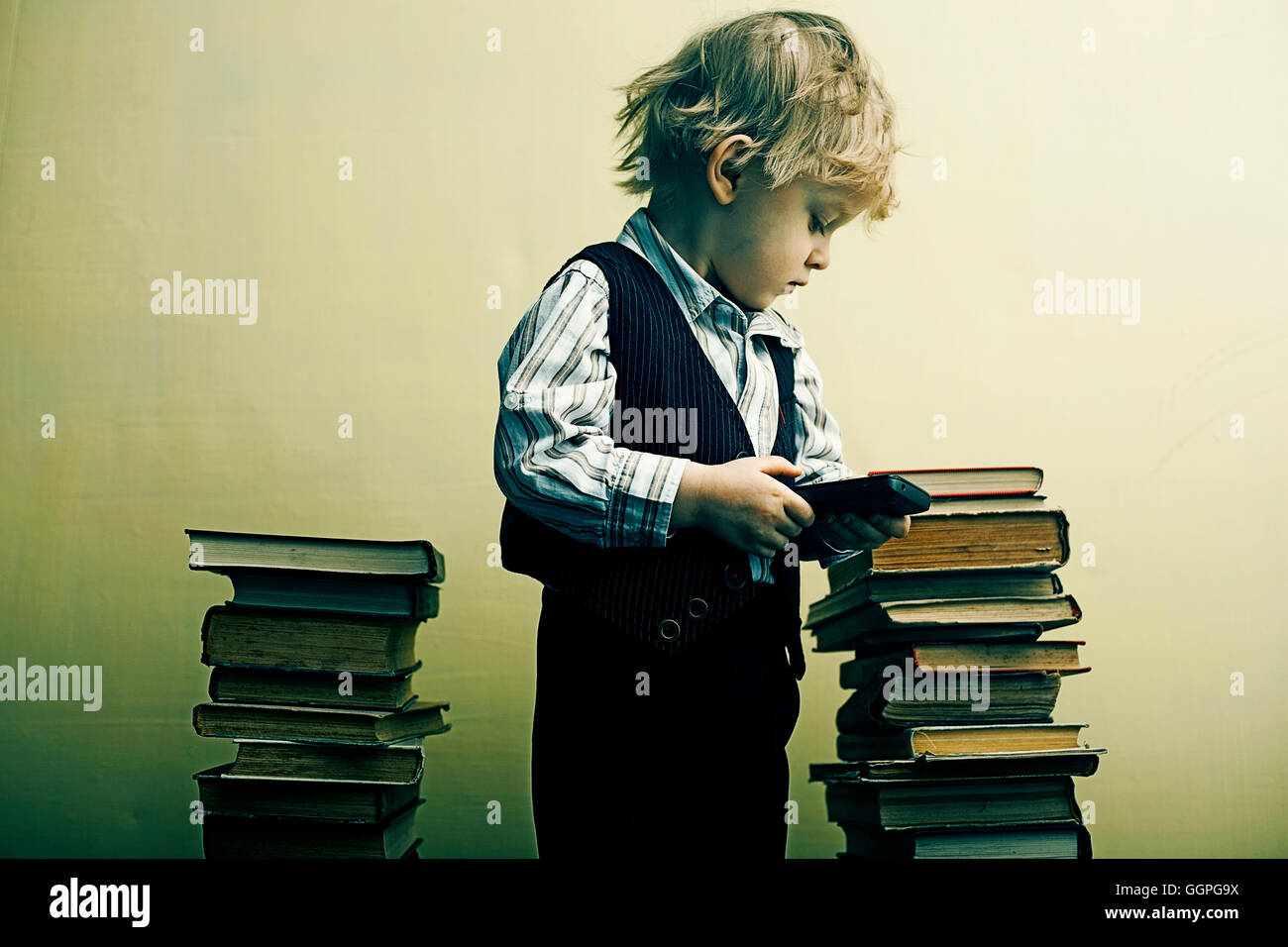 Boy holding cell phone near stacks of books Stock Photo