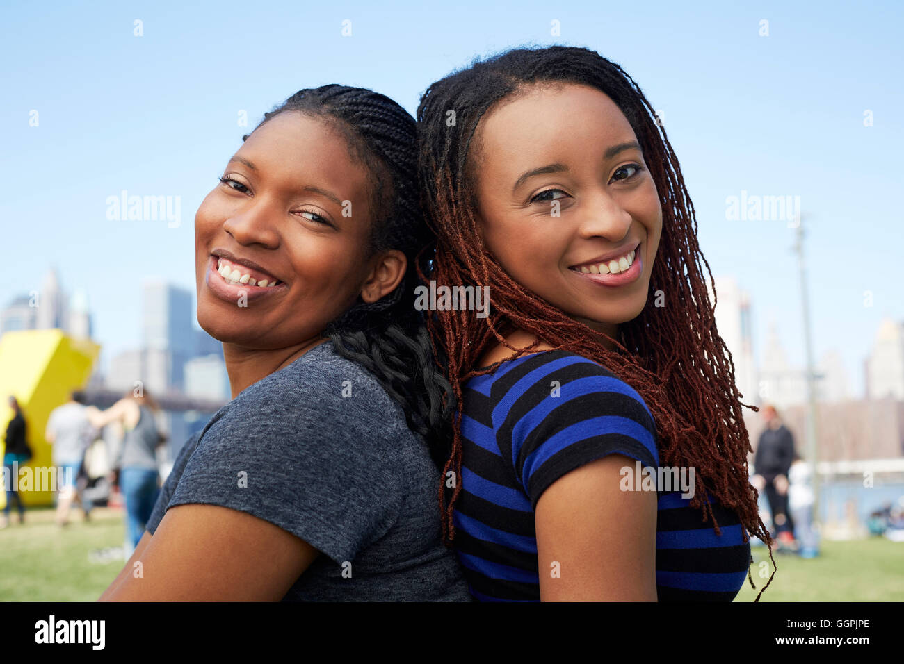 Smiling Black women sitting back to back Stock Photo