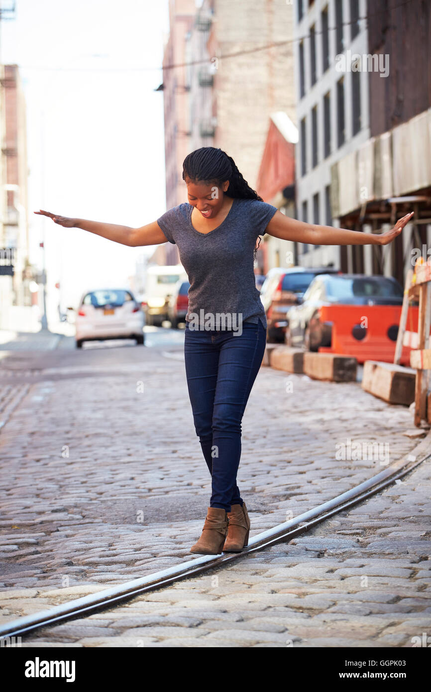 Black woman balancing on track in cobblestone city street Stock Photo ...