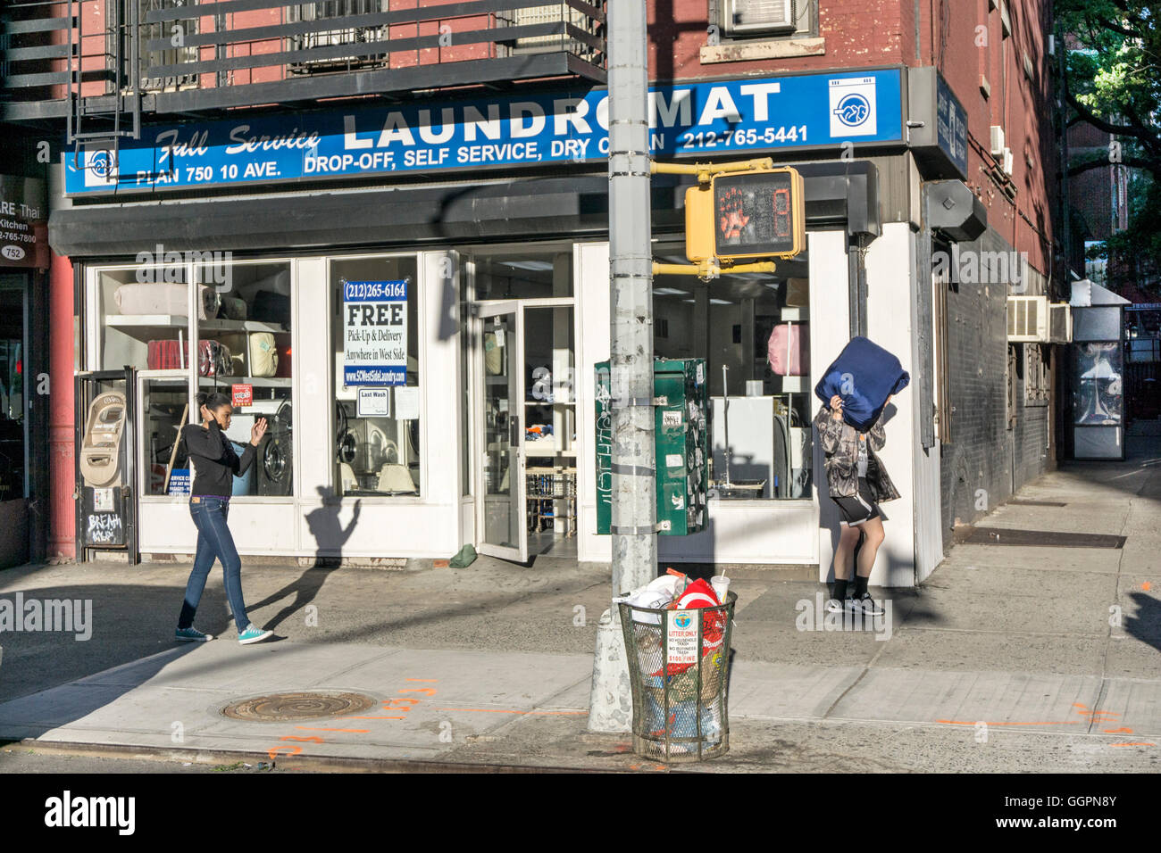 lithe shadow of black teen follows another young pedestrian exiting laundromat at corner of 10th avenue & 51st street Manhattan Stock Photo