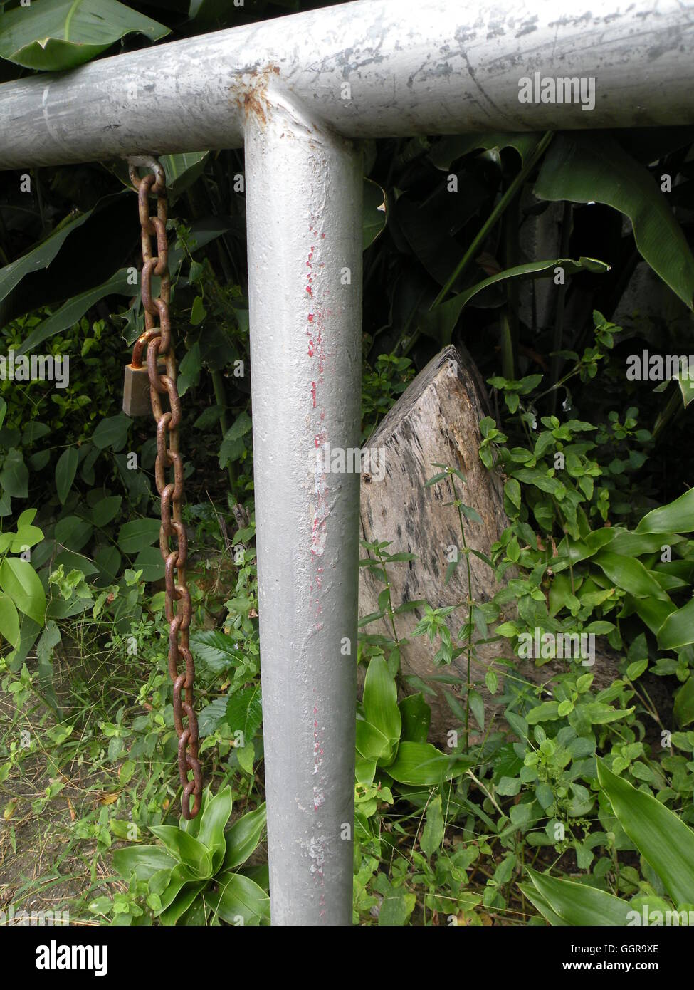 Silver white pipe guard rail hosting a rusty chain and lock, fronting