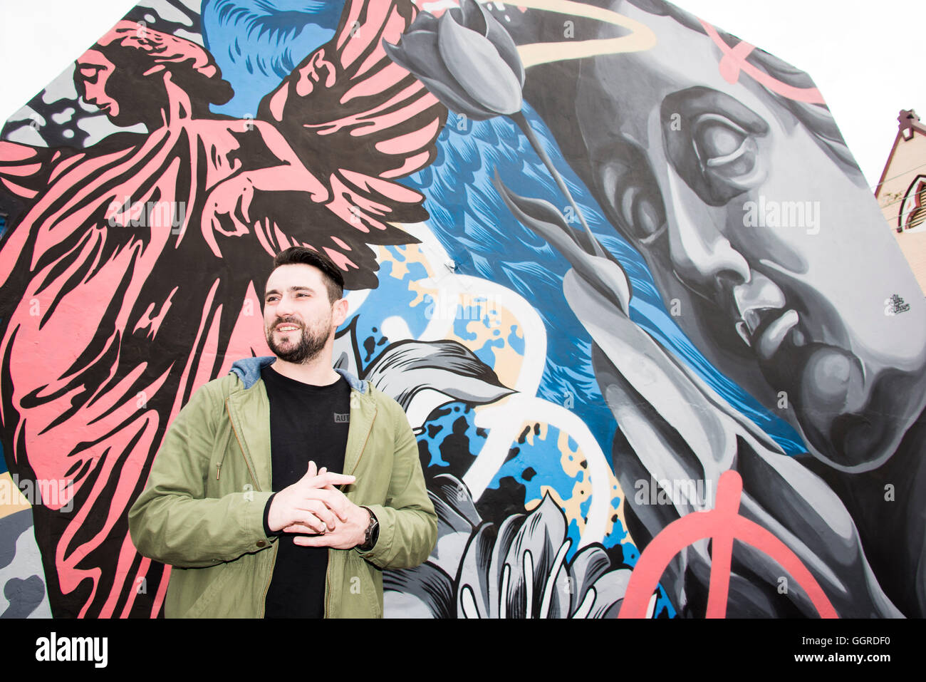 Street artist 'Alex Lehours' poses for a photograph with his newly commissioned street artwork 'The Devine Within' on a terrace house in Newtown  Australia. Perfect Match is a inner city council initiative inviting local property owners to find their Perfect Match by registering interest to have graffitied walls transformed by renowned street artists. © Hugh Peterswald/Alamy Live News Stock Photo