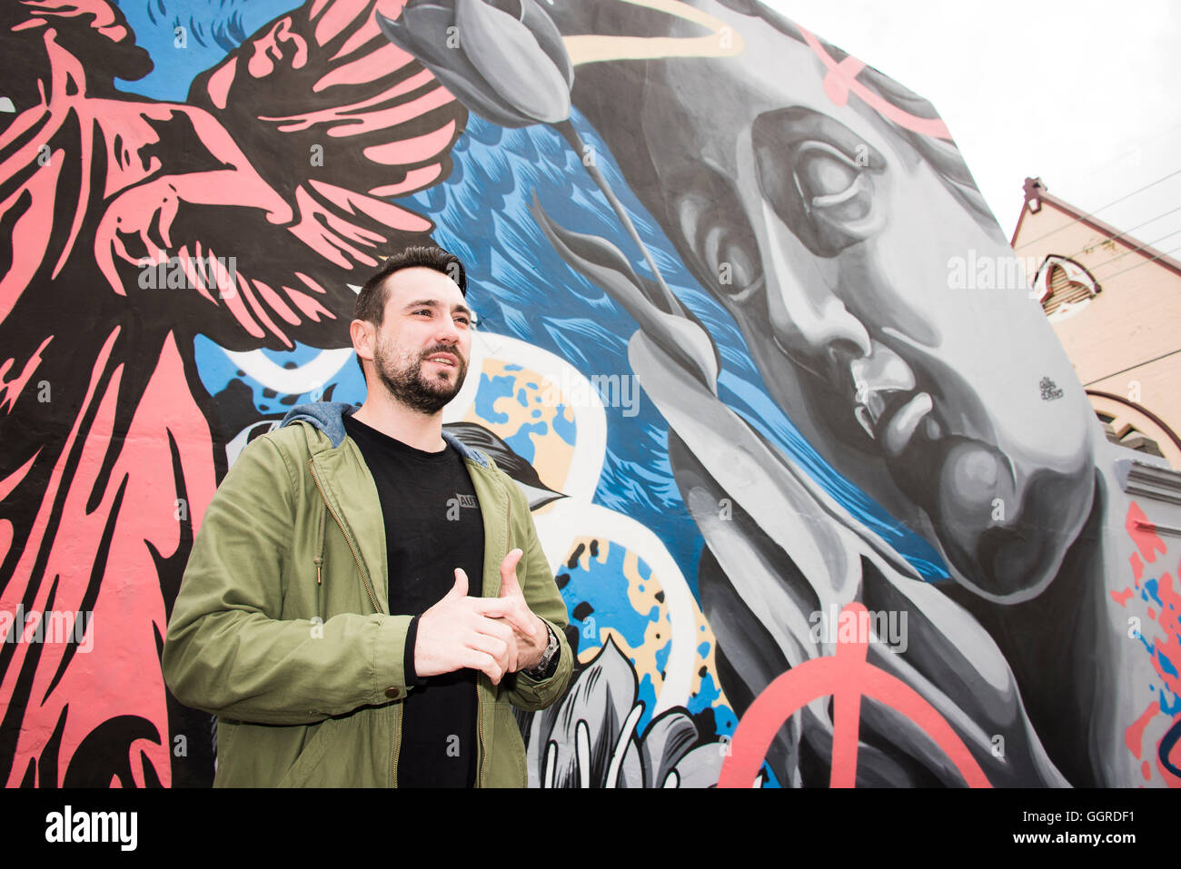 Street artist 'Alex Lehours' poses for a photograph with his newly commissioned street artwork 'The Devine Within' on a terrace house in Newtown  Perfect Match is a inner city council initiative inviting local property owners to find their Perfect Match by registering interest to have graffitied walls transformed by renowned street artists. © Hugh Peterswald/Alamy Live News Stock Photo