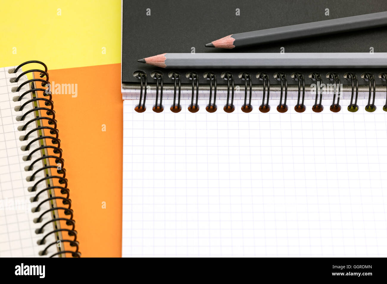 graphite pencils, open multicolor notebooks on yellow surface background closeup Stock Photo