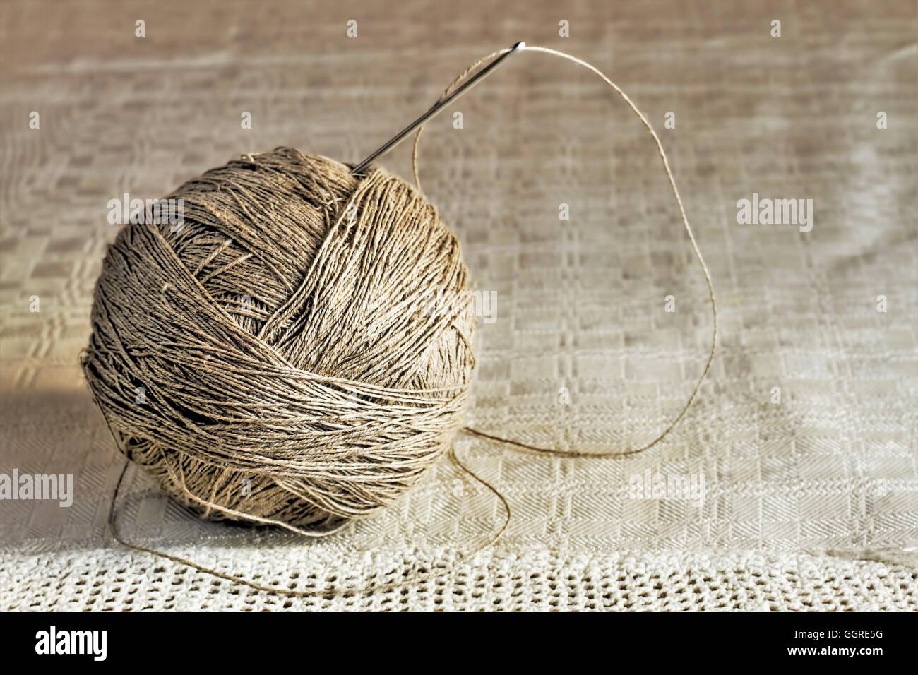 Ball of linen threads with big needle on handmade gray tablecloth