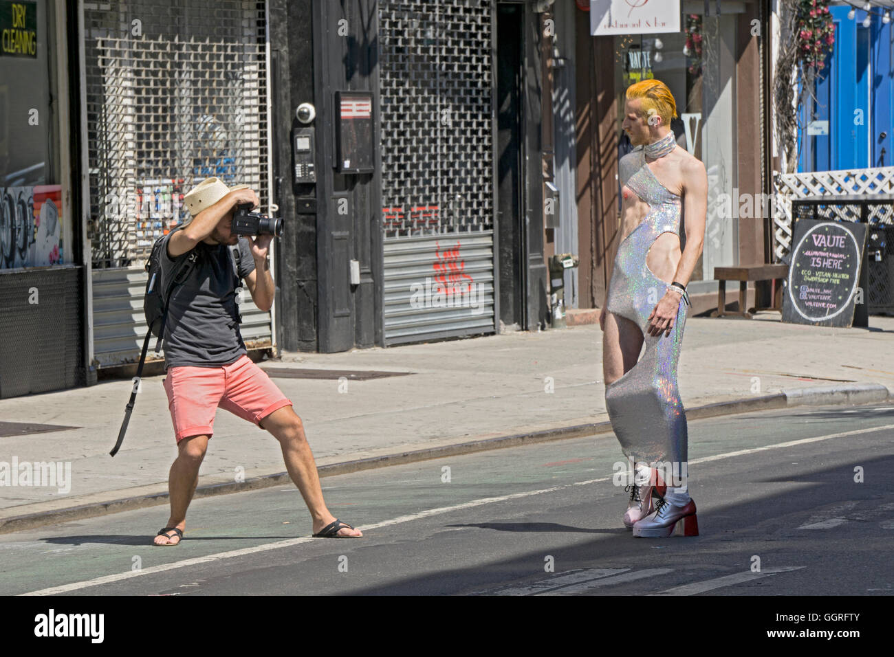 A photographer taking pictures of a man with gold hair in a long sparkling dress on Ludlow St. in Lower Manhattan, New York City Stock Photo