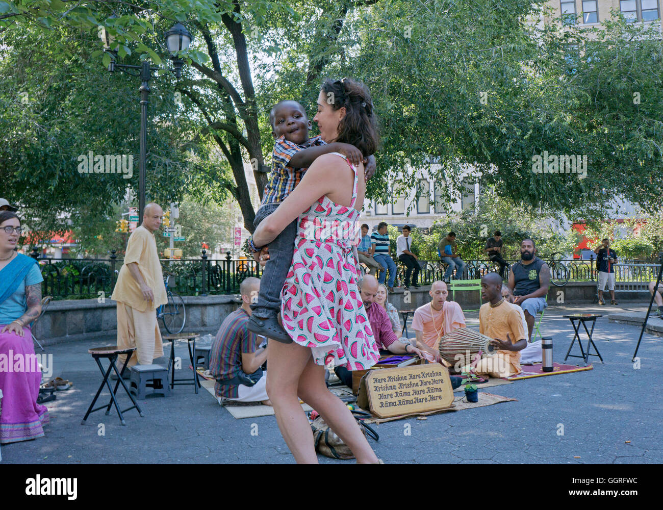 A pretty Caucasian lady dancing with a young African American child in front of Hare Krisna musicians in Union Square Park, NYC Stock Photo