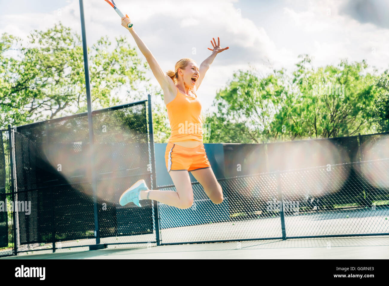 Caucasian woman jumping for joy on tennis court Stock Photo
