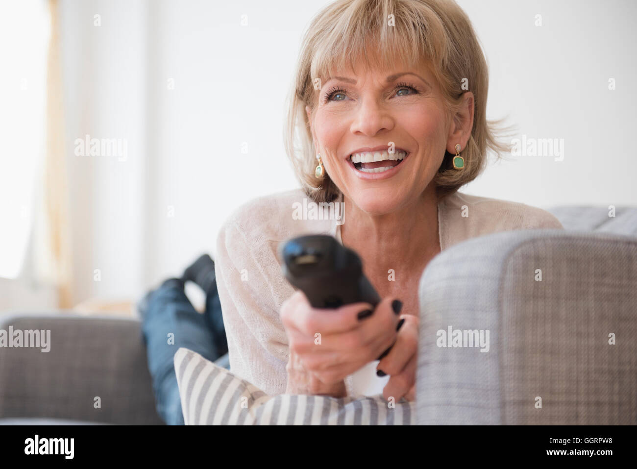 Older Caucasian woman laying on sofa watching television Stock Photo