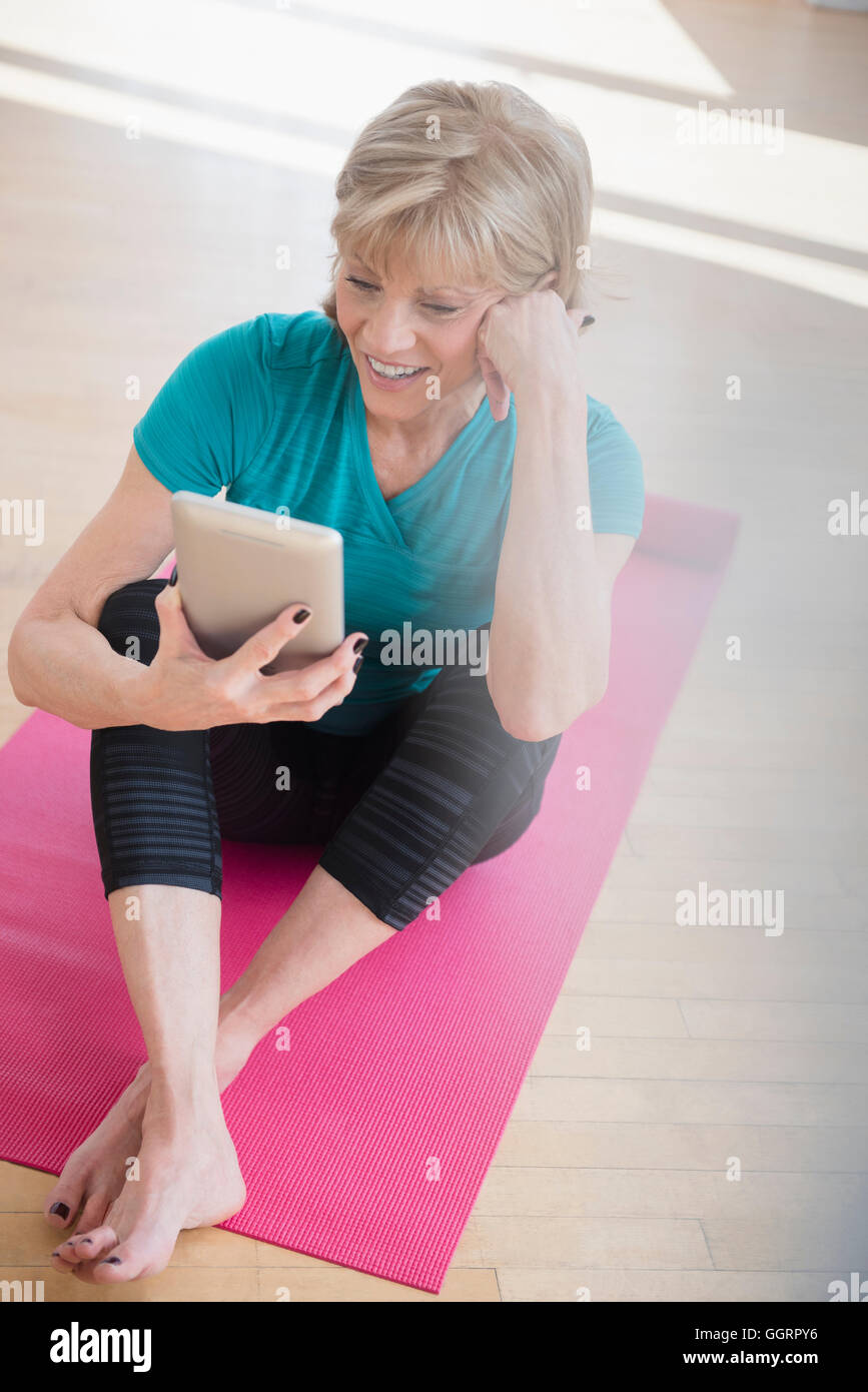 Older Caucasian woman on exercise mat using digital tablet Stock Photo