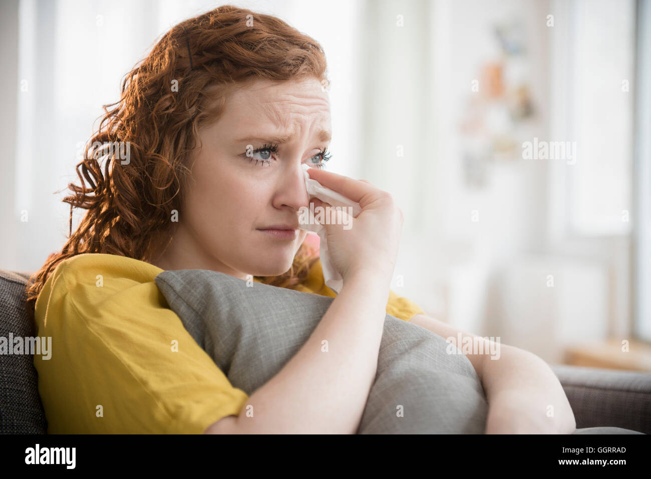 Crying Caucasian woman clutching pillow wiping tears Stock Photo