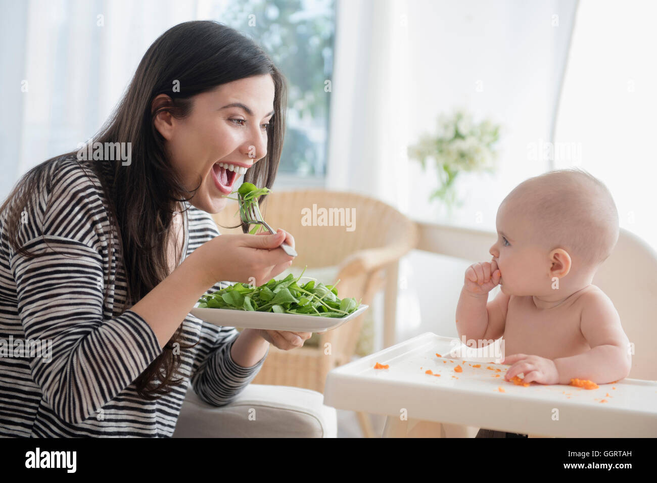 Caucasian woman eating salad while watching baby daughter Stock Photo