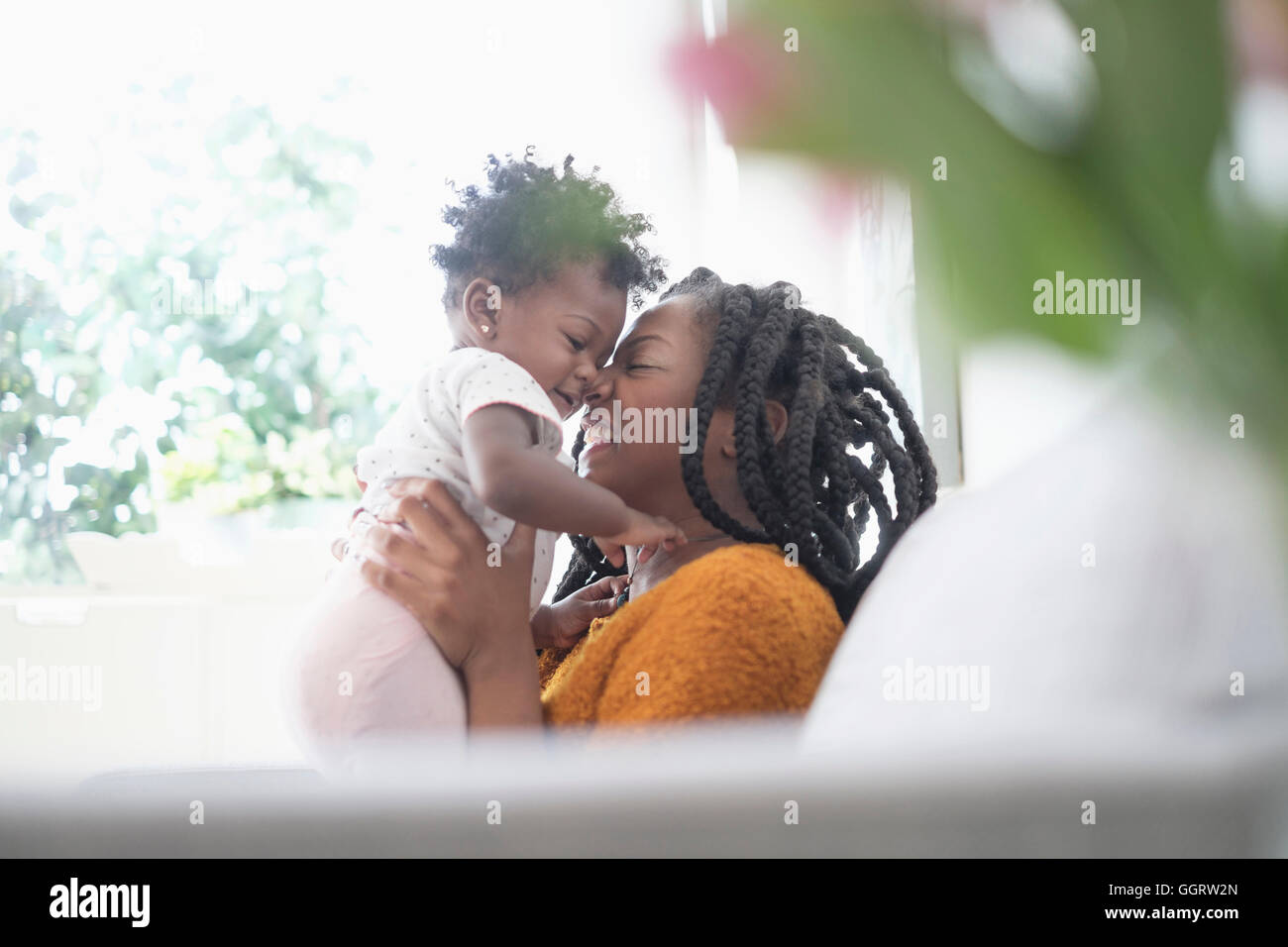 Black woman rubbing noses with baby daughter on sofa Stock Photo