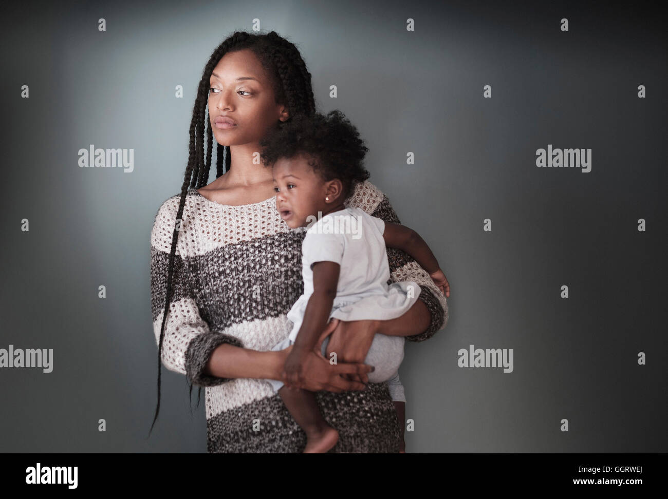 Thoughtful Black woman standing holding baby daughter Stock Photo