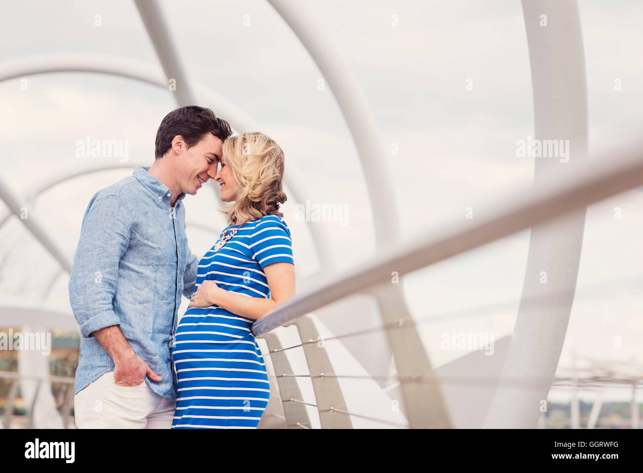 Smiling Caucasian man and expectant mother rubbing noses on walkway Stock Photo