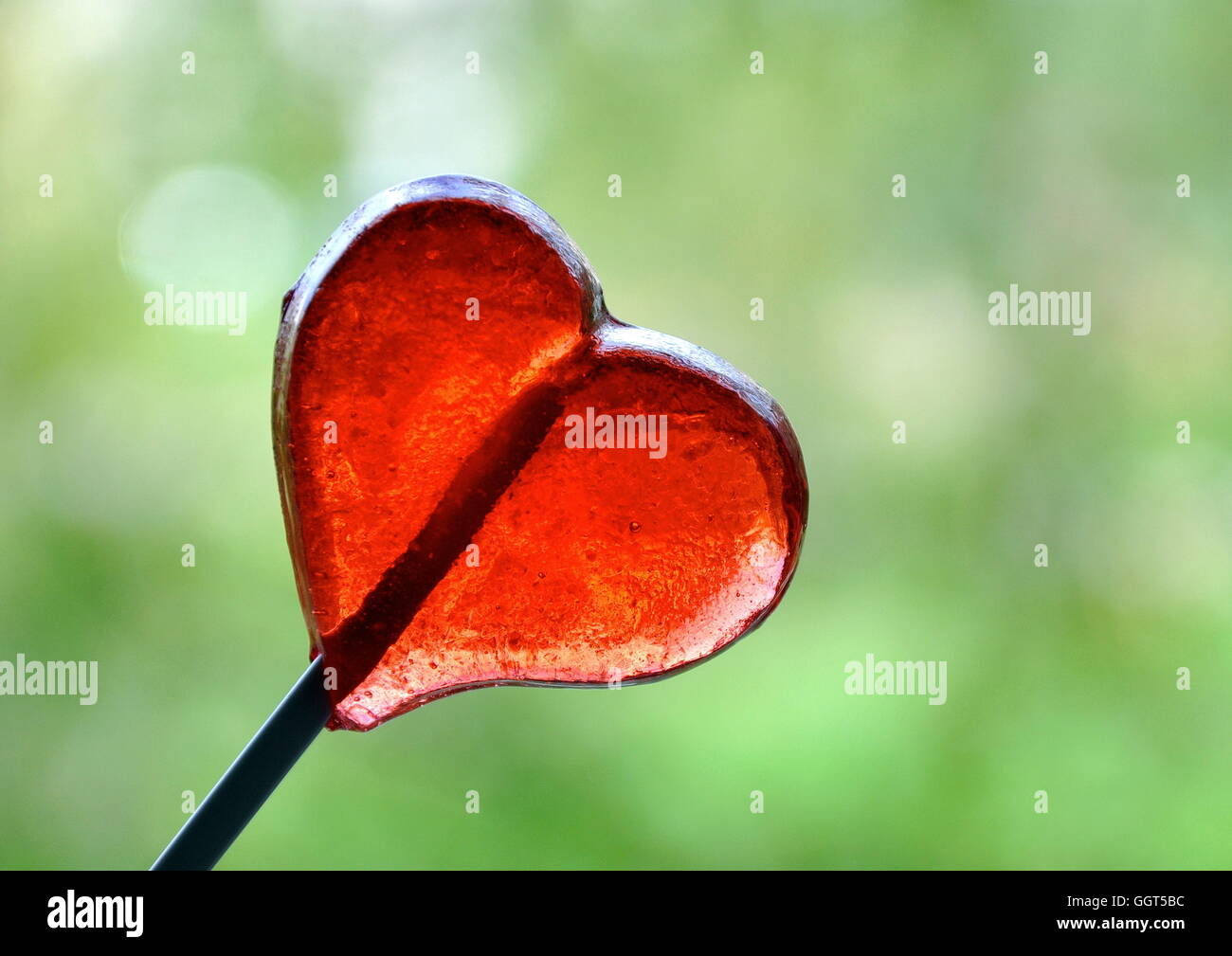 Heart-shaped red lollypop on a green background Stock Photo - Alamy