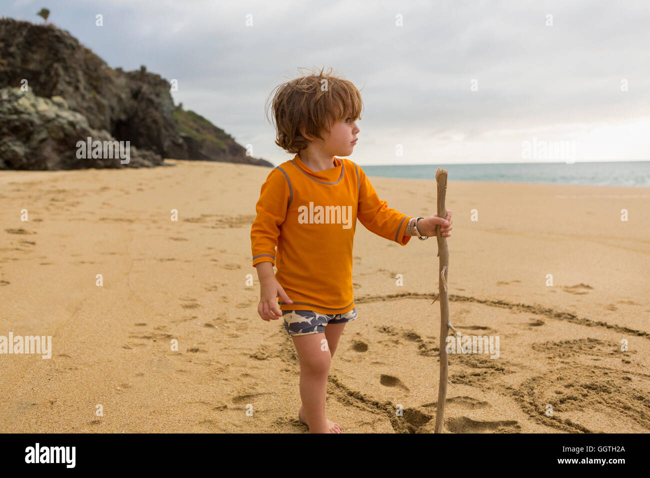 Caucasian boy with walking stick on beach Stock Photo