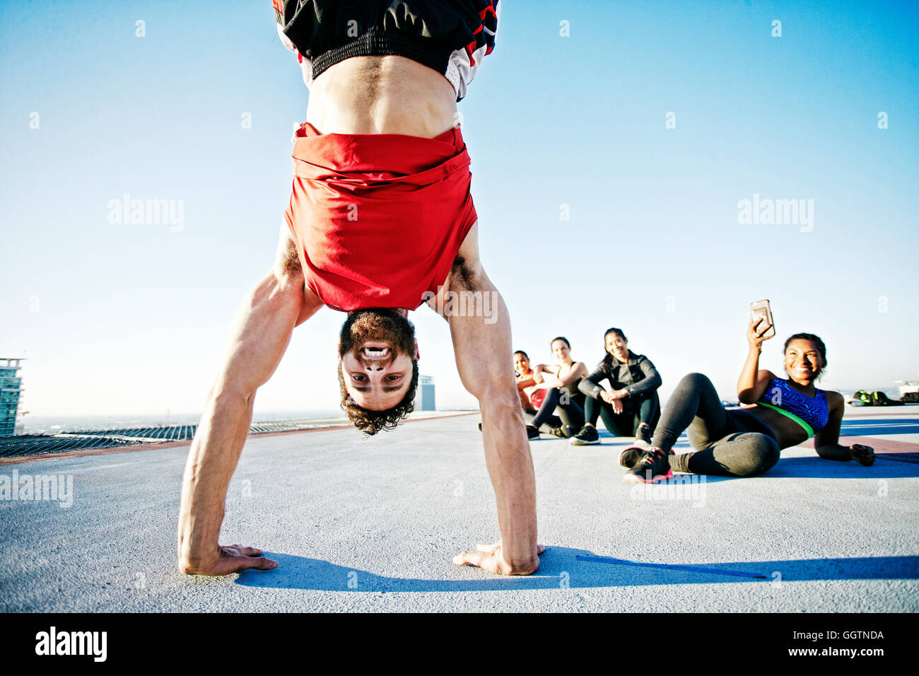 Woman photographing man doing handstand on urban rooftop Stock Photo