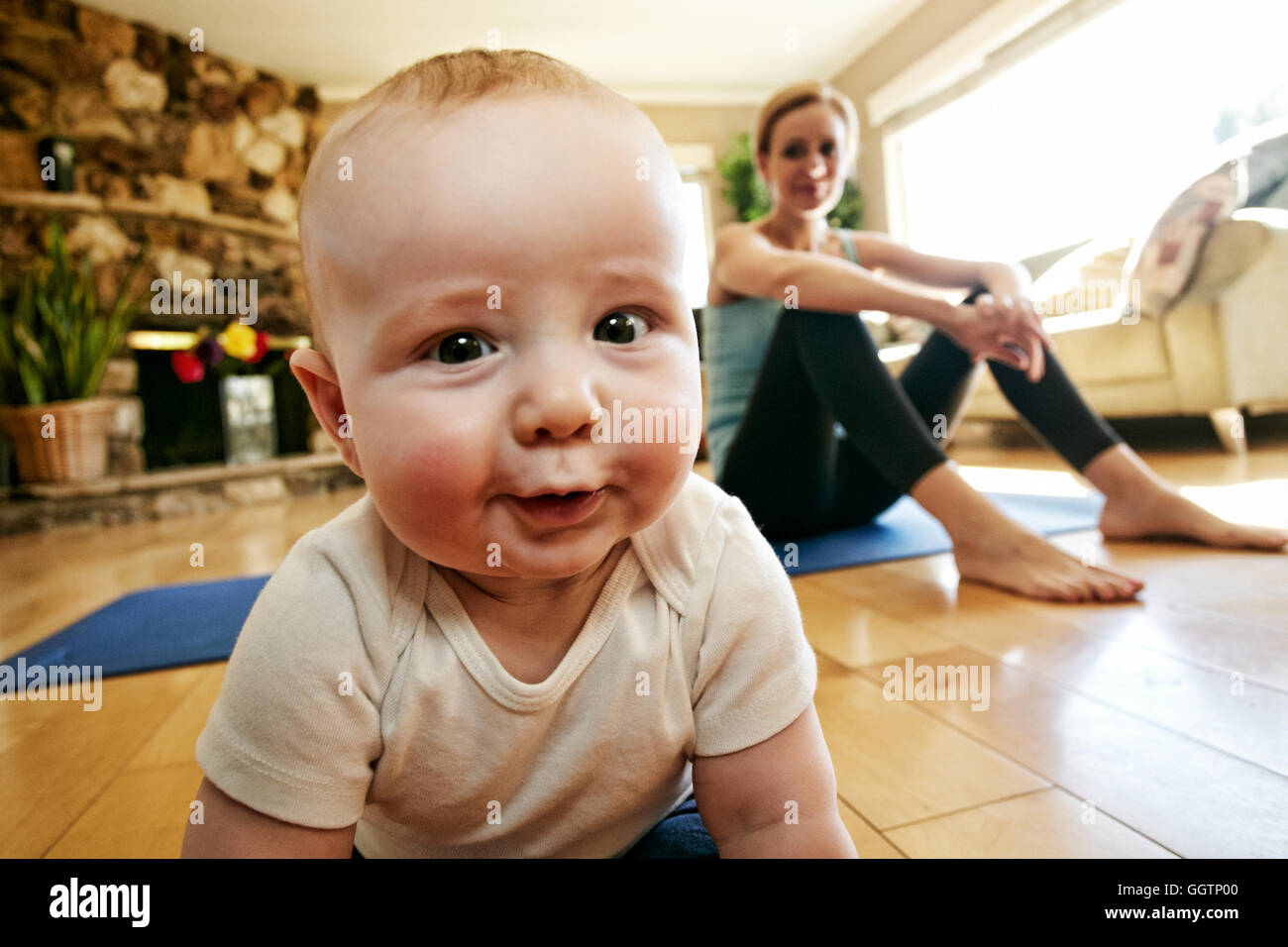 Baby crawling on floor while mother rests from workout Stock Photo