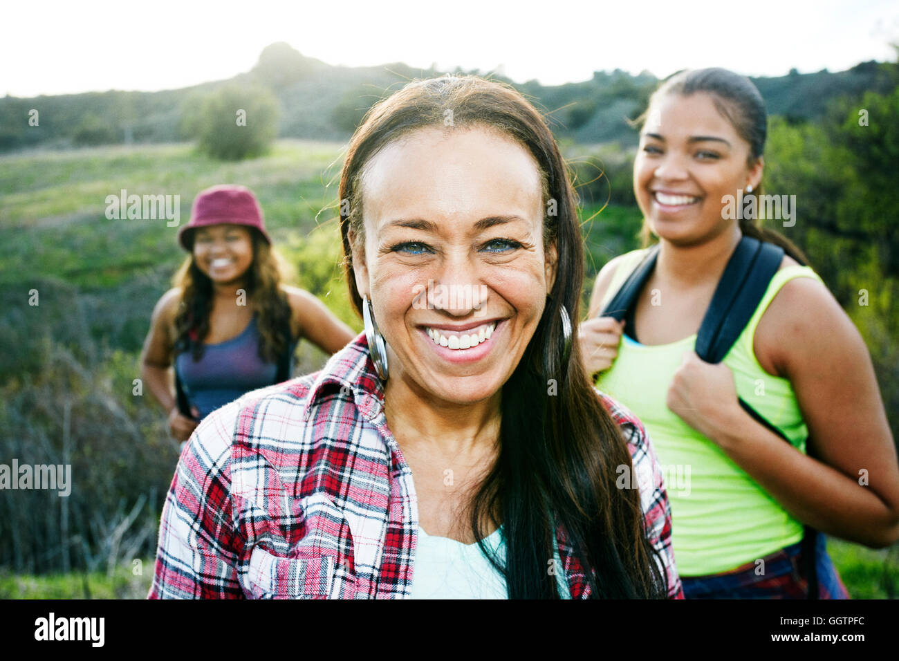 Mixed Race mother and daughters backpacking in field Stock Photo