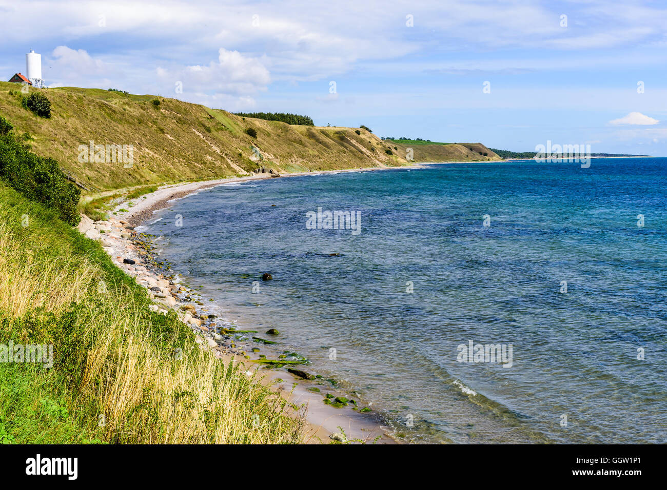 Sandy coastal slopes covered in dry grass in an ocean bay. White silo at a farm visible. Southern Skane in Sweden. Stock Photo