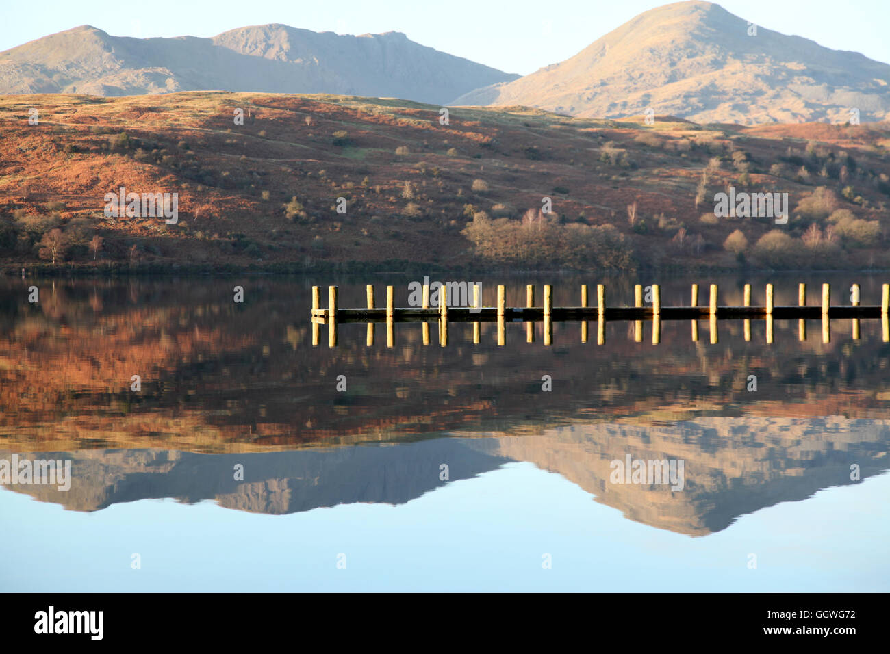 A wooden jetty crosses the reflection of a Lakeland mountain on Coniston water in winter Stock Photo