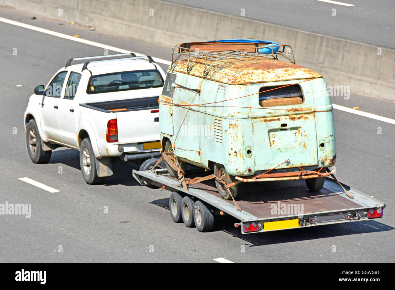 Towing rusty old van on trailer being transported along UK motorway England by pickup truck obscured numberplates Stock Photo