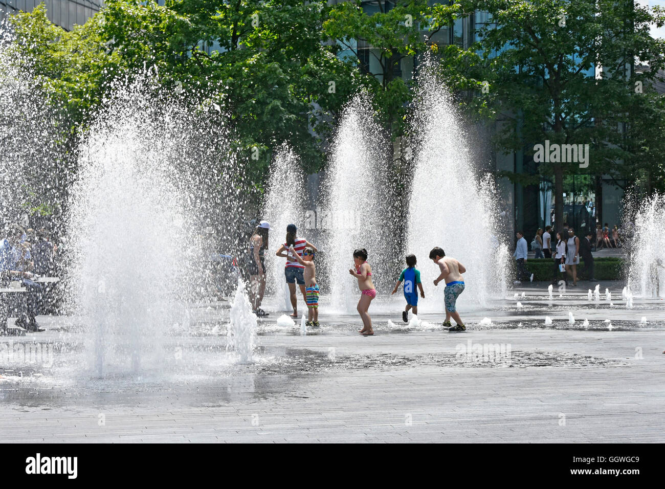 Children playing in variable height water fountain jets at random timings during hot summer weather ideal for kids outdoors London England UK Stock Photo