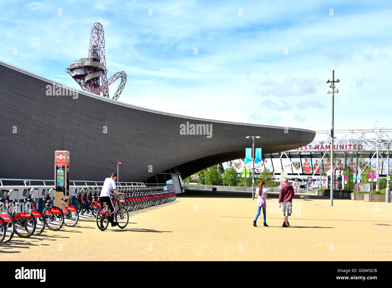 Person riding from Santander bike hire docking station at Aquatic Centre with Orbit Tower beyond in Queen Elizabeth Olympic Park Stratford London UK Stock Photo