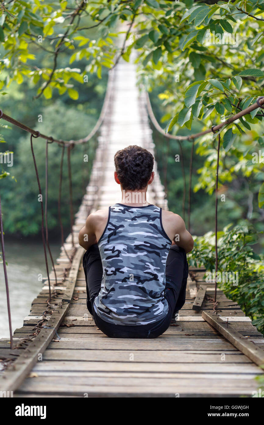 Teenager boy sitting on a wooden bridge over the river Stock Photo - Alamy