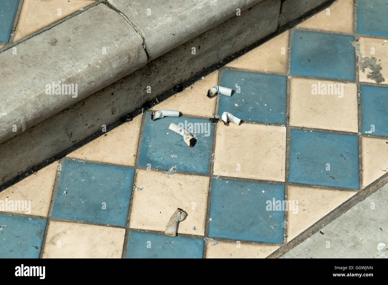 Cigarette butts on tiled step of old house. Stock Photo