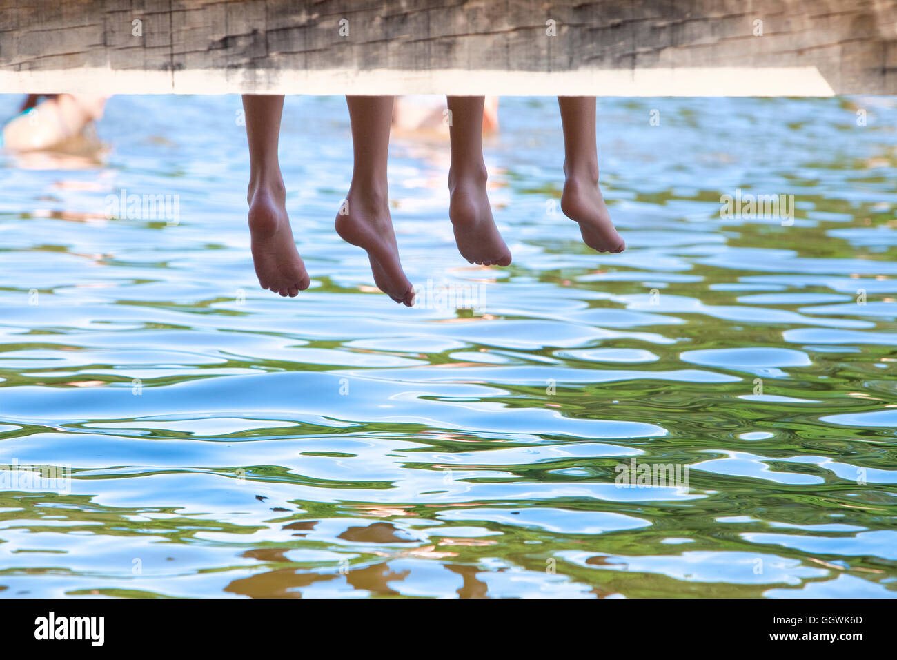 Boys Legs Dangling Down from Wooden Pier over Water Stock Photo