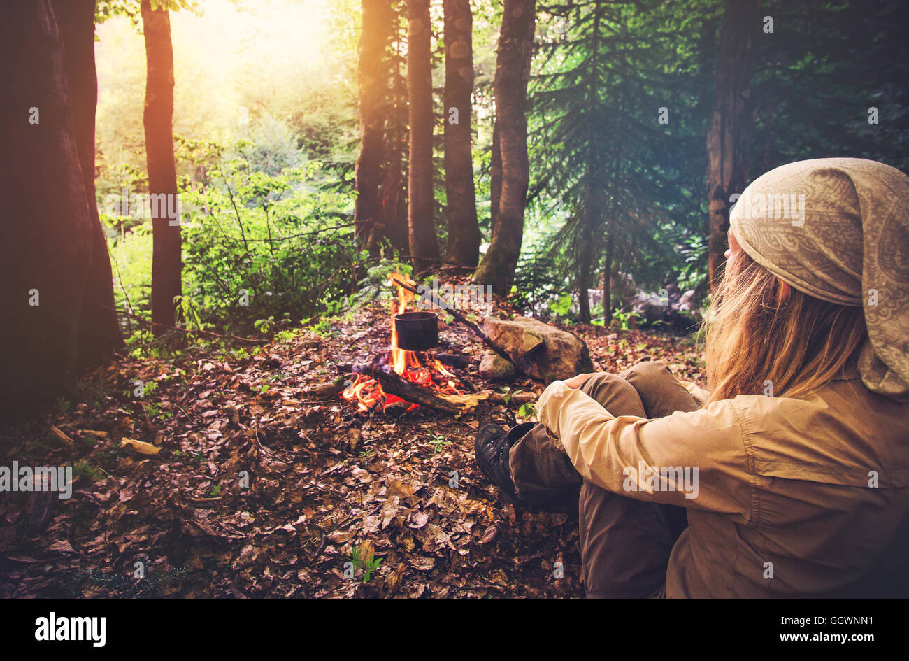 Woman traveler relaxing in forest and cooking food in kettle on fire Travel Lifestyle concept vacations outdoor picnic bivouac i Stock Photo