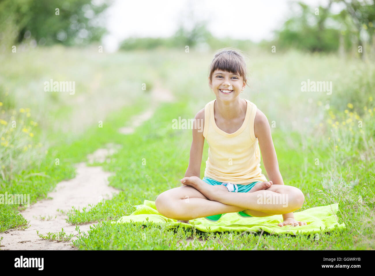 Young girl smiling while sitting in lotus position outdoors Stock Photo