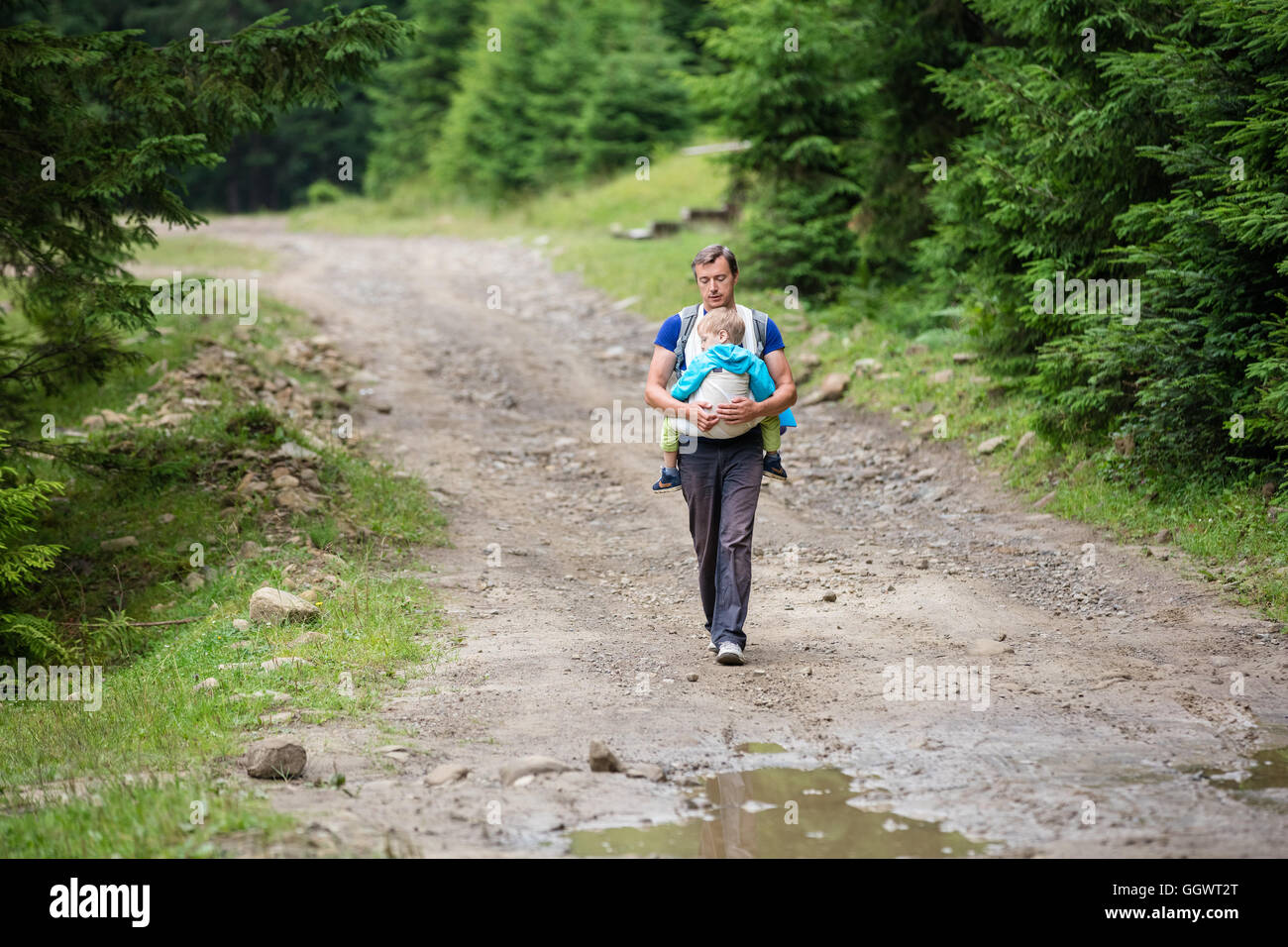 Caucasian man carrying his sleeping son in wrap sling while hiking