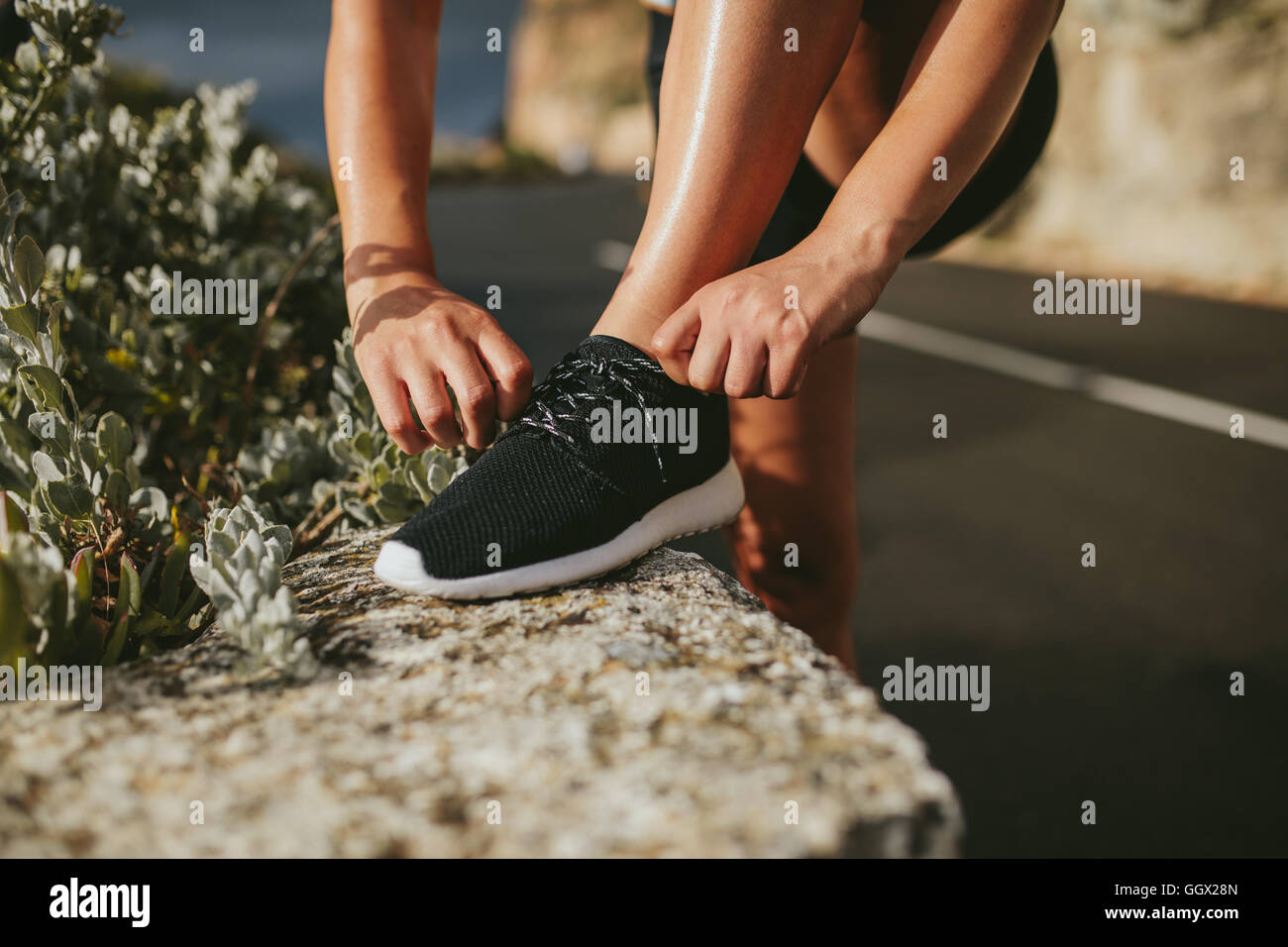 Woman lacing running shoes before workout outdoors on countryside road. fitness and healthy lifestyle concept. Stock Photo