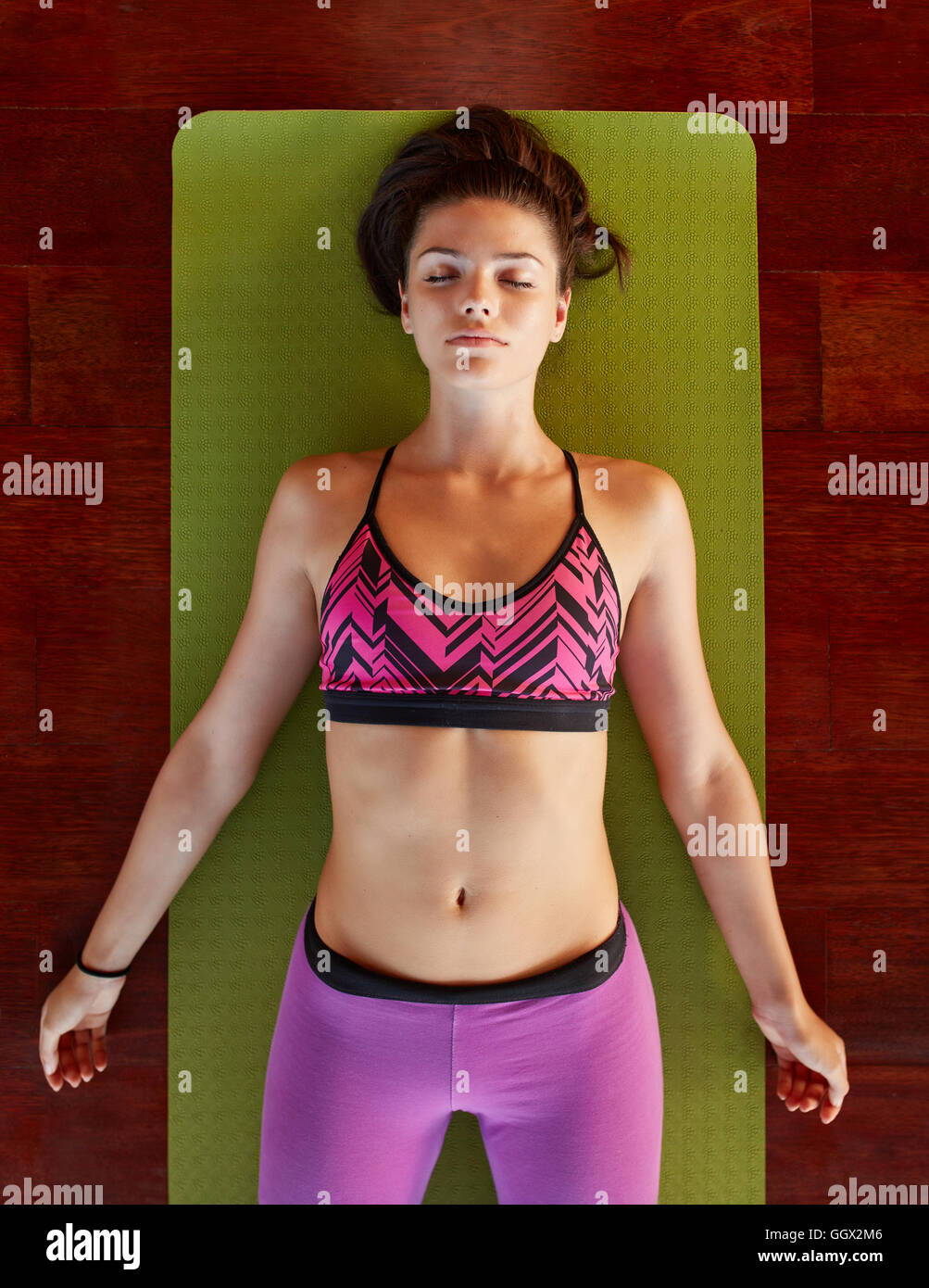 Overhead view of fit young female relaxing on yoga mat. Healthy woman in savasana yoga pose at gym. Stock Photo