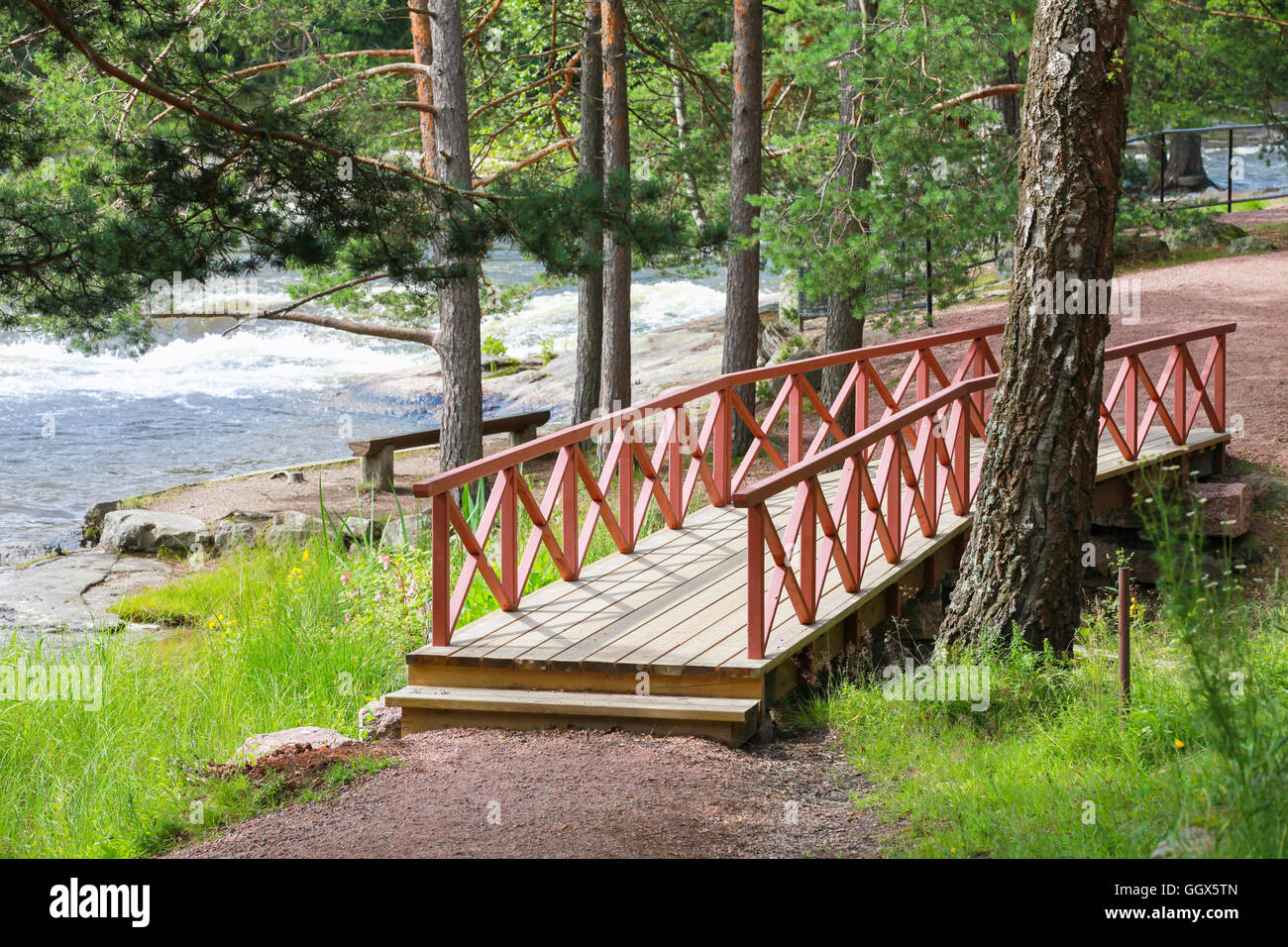 Small wooden bridge with red railings over stream in summer park. Kotka, Finland Stock Photo