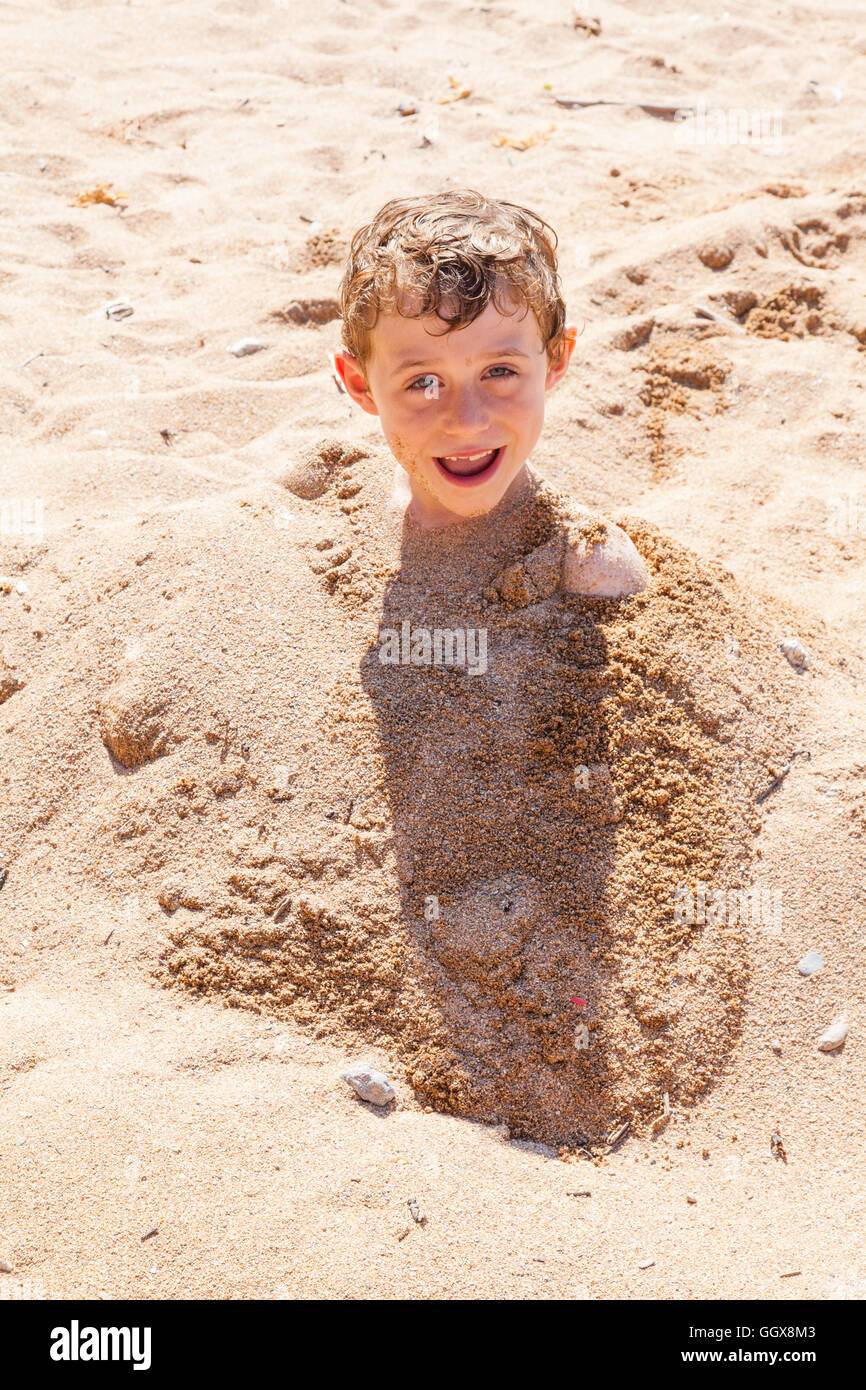 Six year old boy buried in the sand , Hope Cove, Devon, England, United Kingdom Stock Photo
