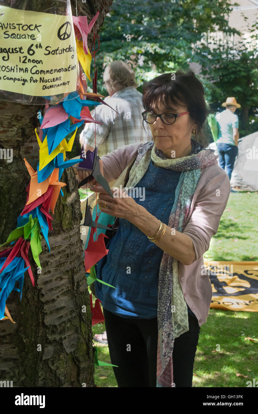 London, UK. 6th August 2016. A woman fixes peace cranes on the commemorative cherry tree at the CND ceremony in memory of the victims, past and present on the 71st anniversary of the dropping of the atomic bomb on Hiroshima and the second atomic bomb dropped on Nagasaki three days later. Peter Marshall/Alamy Live News Stock Photo