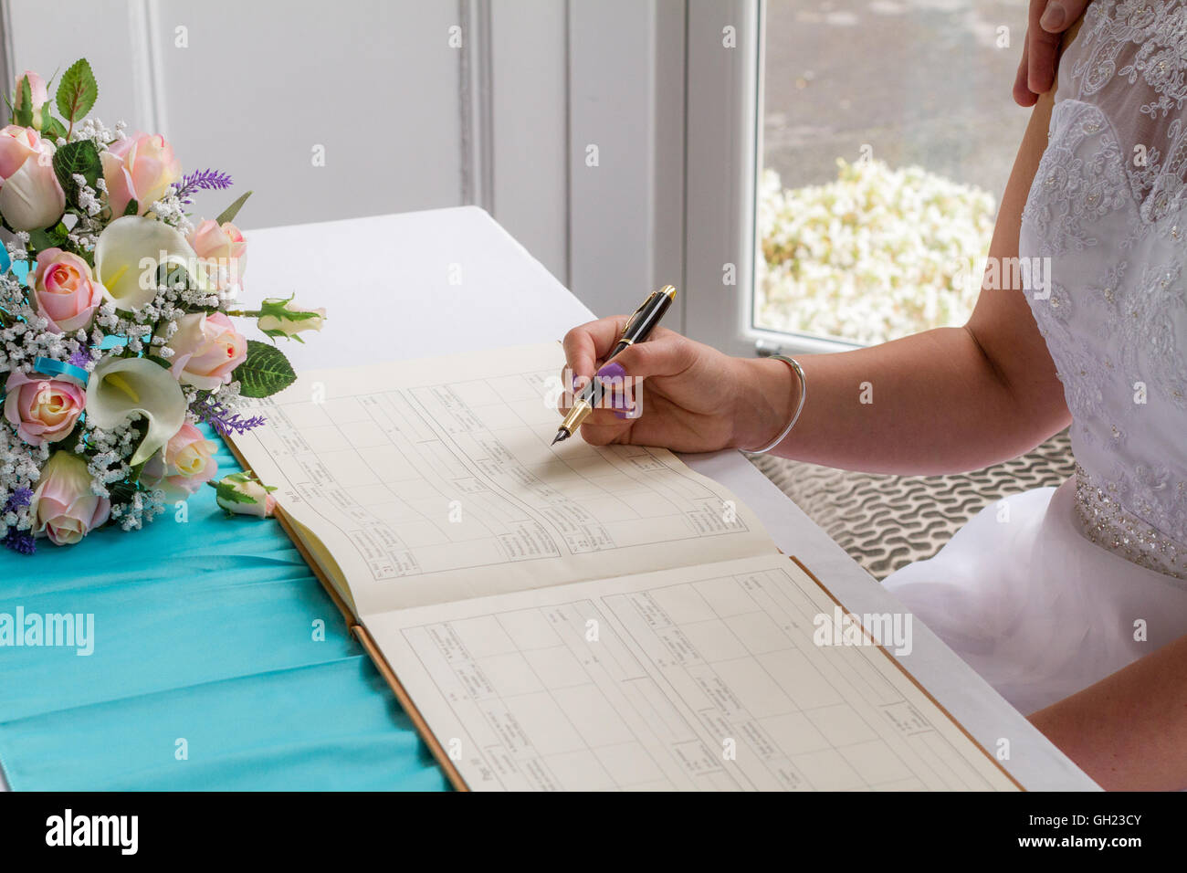The bride signing the register at her wedding day to confirm her marriage. Stock Photo