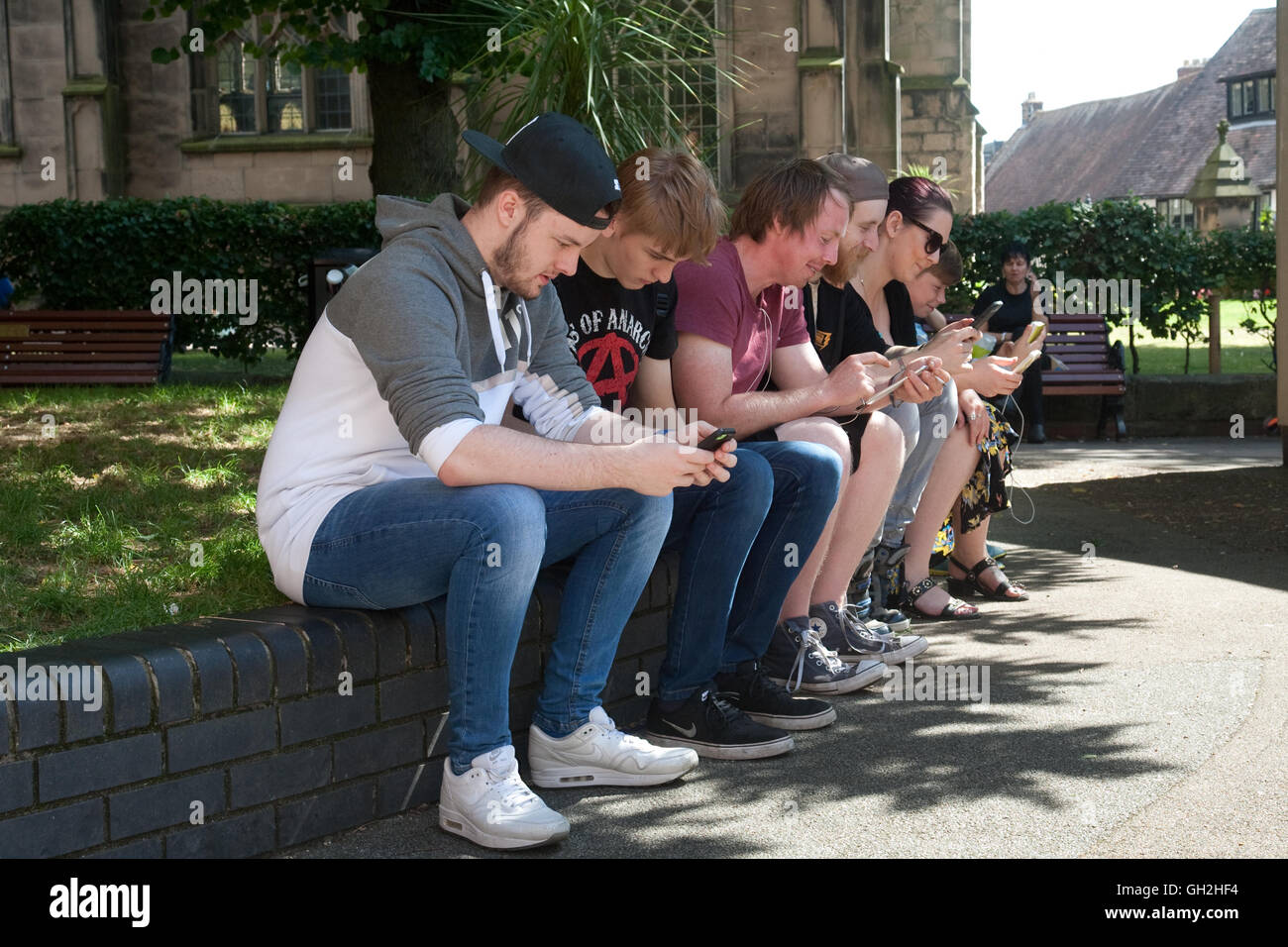 A group of people, male and female, checking the internet, social media etc on their mobile phones in public. Shrewsbury, Shropshire, summer 2016 Stock Photo